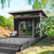 Modern studio shed with glass double doors, transom windows, and a wooden overhang on a raised deck with seating.