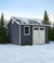 Heartland storage shed shown in backyard with fence, pine trees and snow