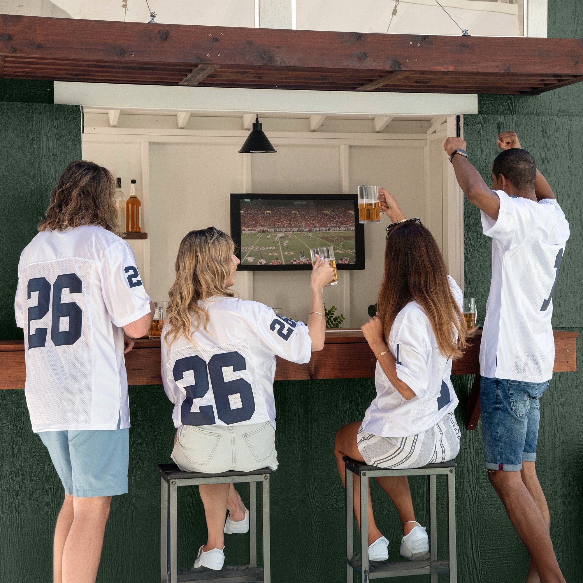 People enjoying a football game inside the Pentwater Bar Shed with a TV setup, creating the perfect space for outdoor entertainment