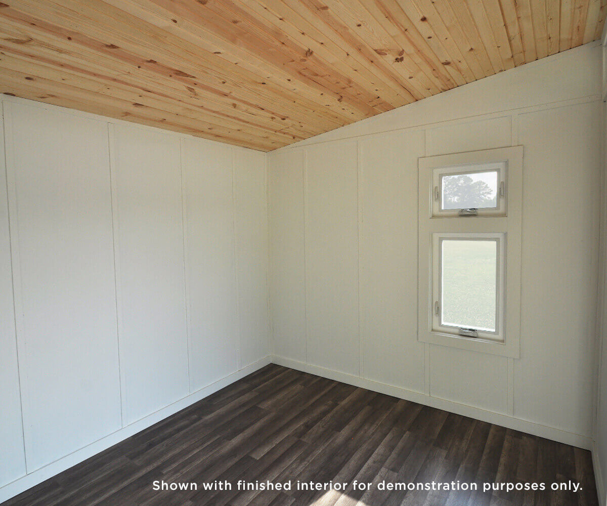 Finished interior of a studio shed with wood ceiling, white walls, and a double-pane window for natural light.